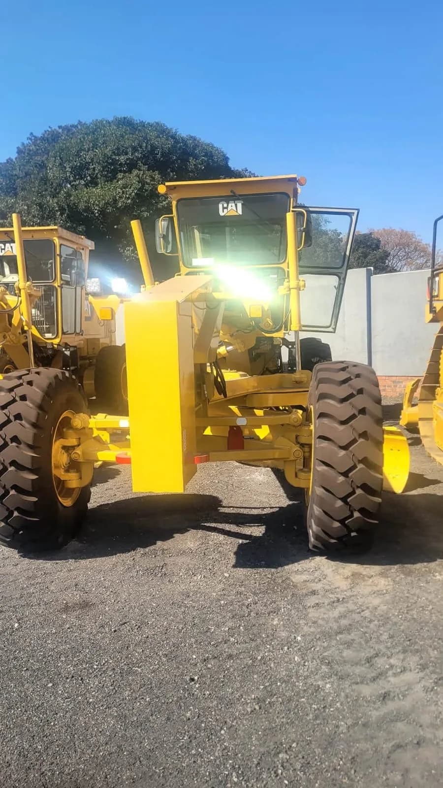 A yellow Caterpillar motor grader parked on open ground.