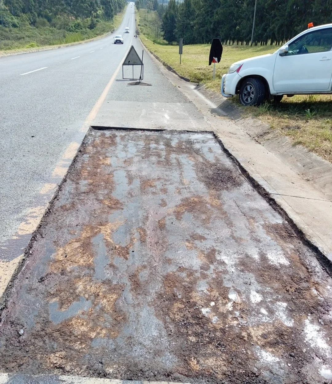 A prepared road patch with a warning triangle and a chevron board standing beyond it.
