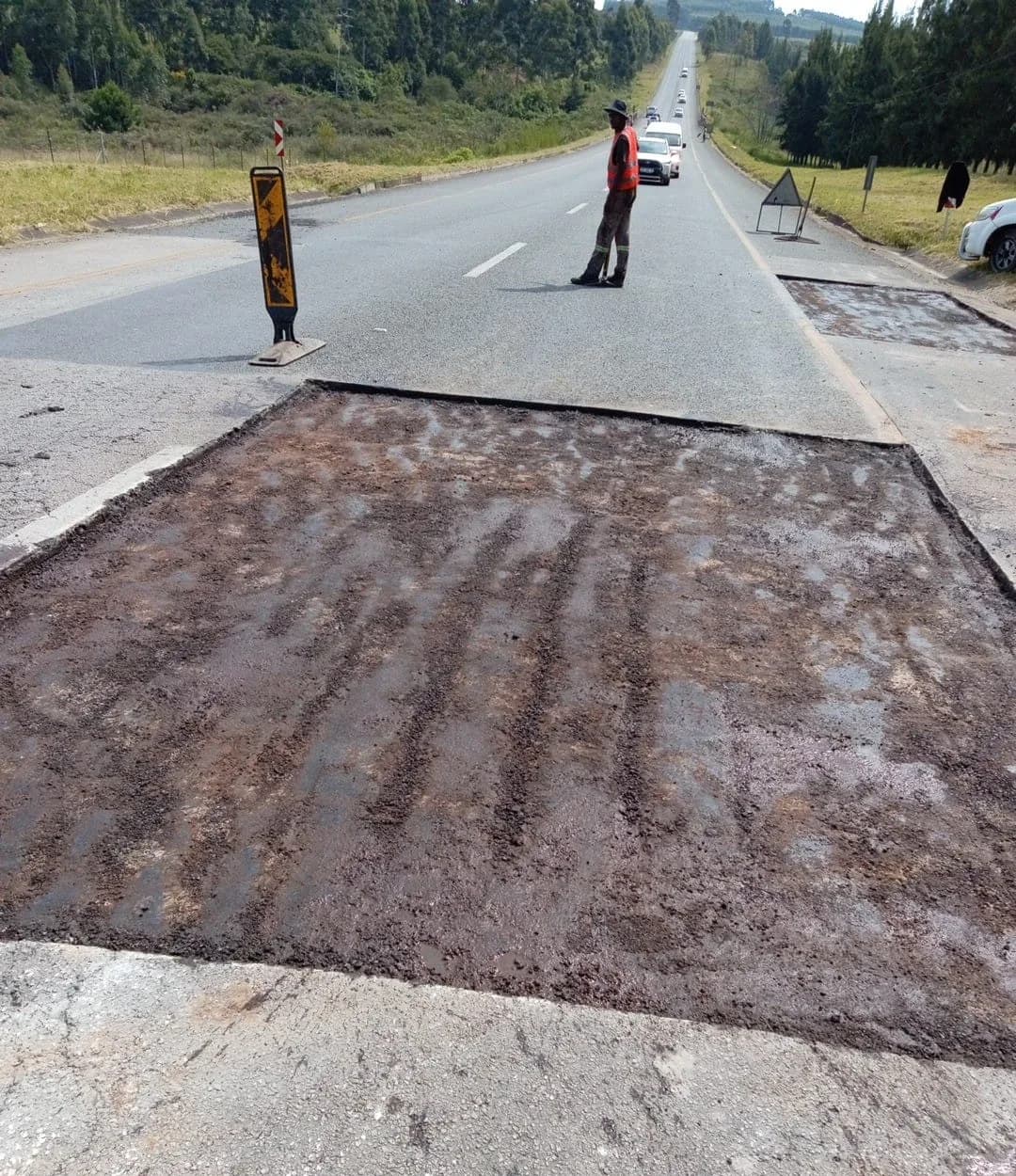 A prepared patch in the foreground with a flagman controlling traffic further up the road.