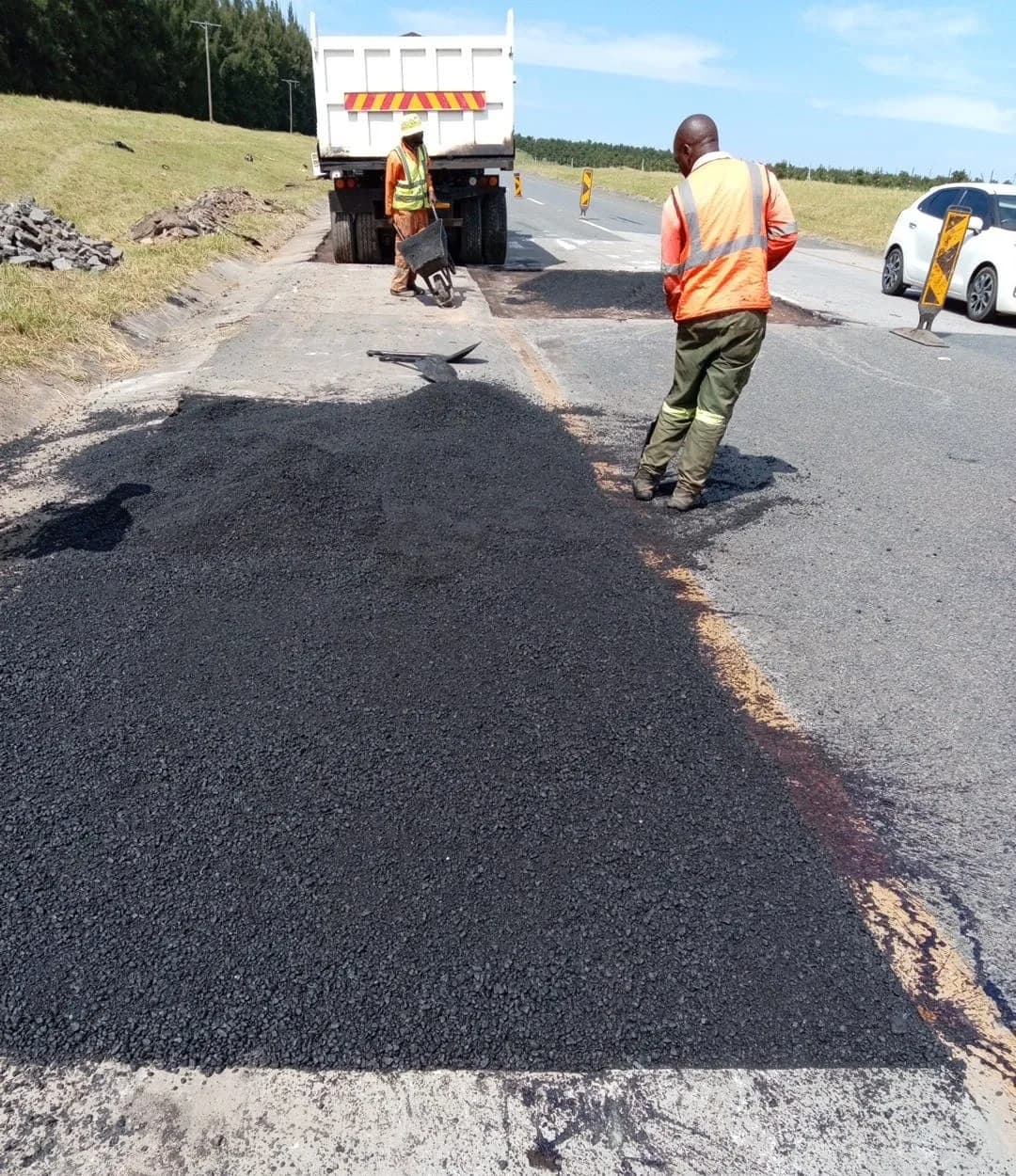 Fresh asphalt being spread by rake into a prepared road patch.