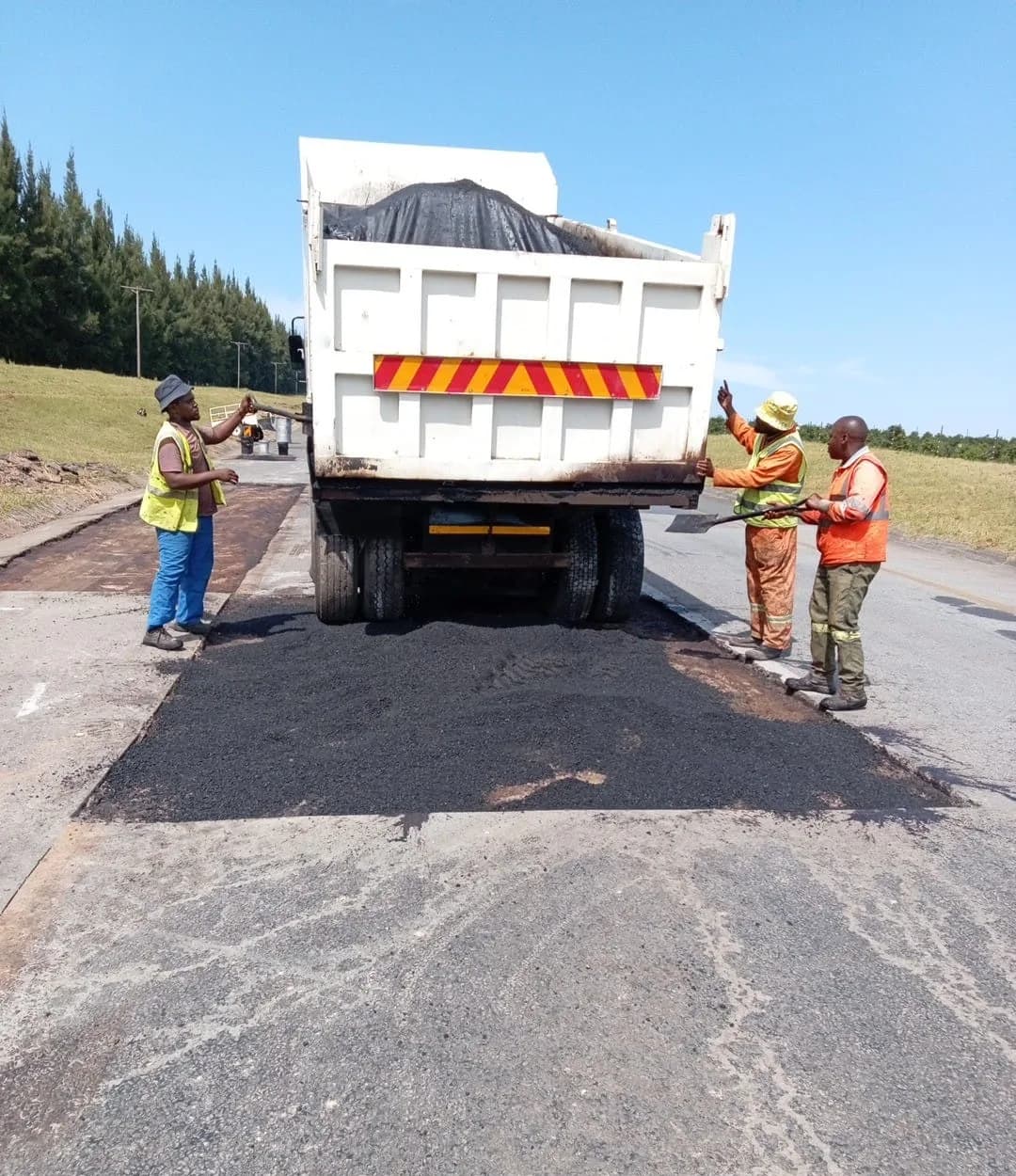 A tipper truck discharging asphalt while crew members spread it with shovels.