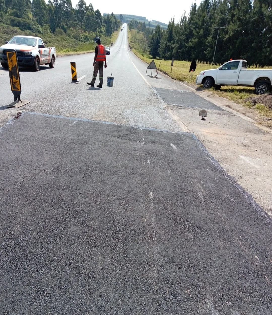 A finished, flush road patch with a flagman and warning boards still standing.